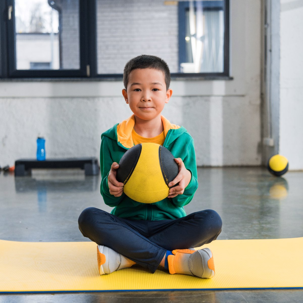 Asian boy holding a ball on an exercise mat.